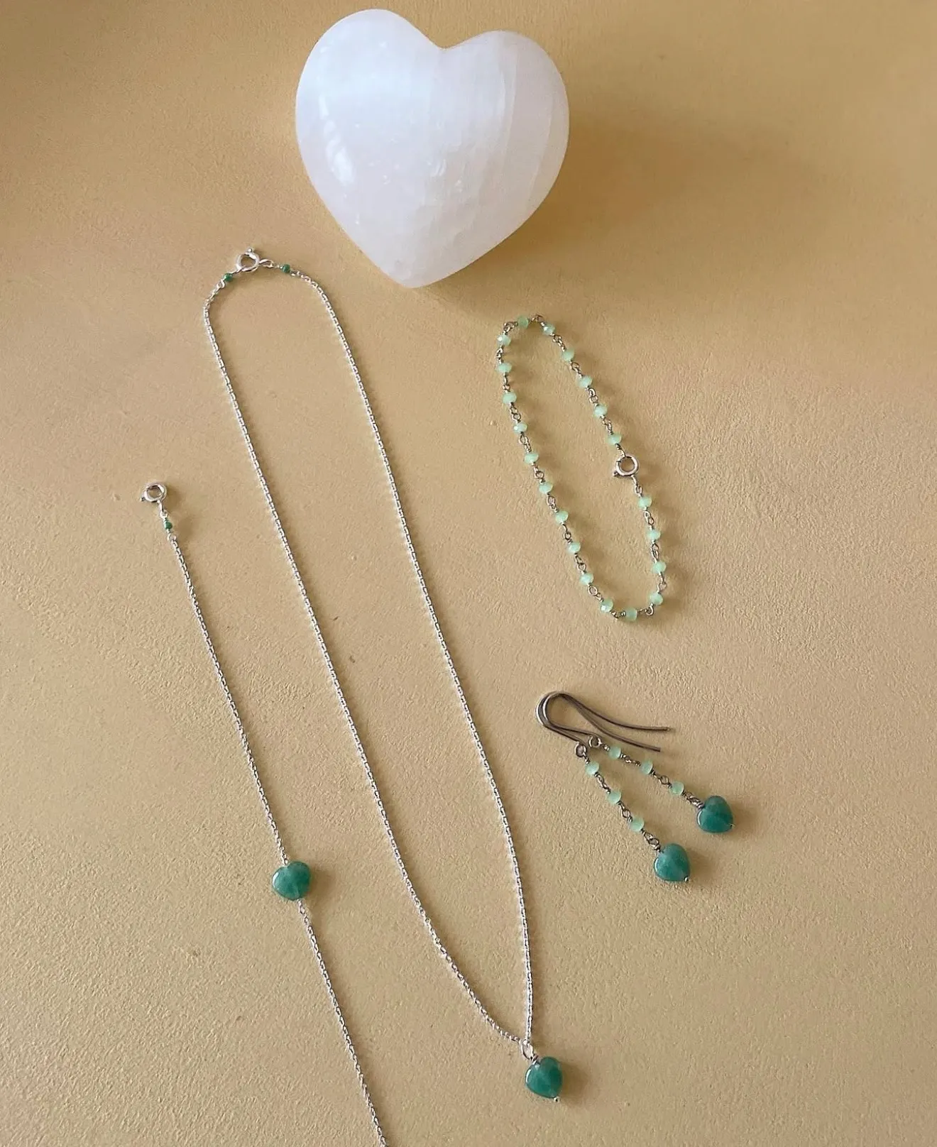 Collar, pulsera y pendientes de plata con pequeños corazones de piedra verde sobre fondo de arena